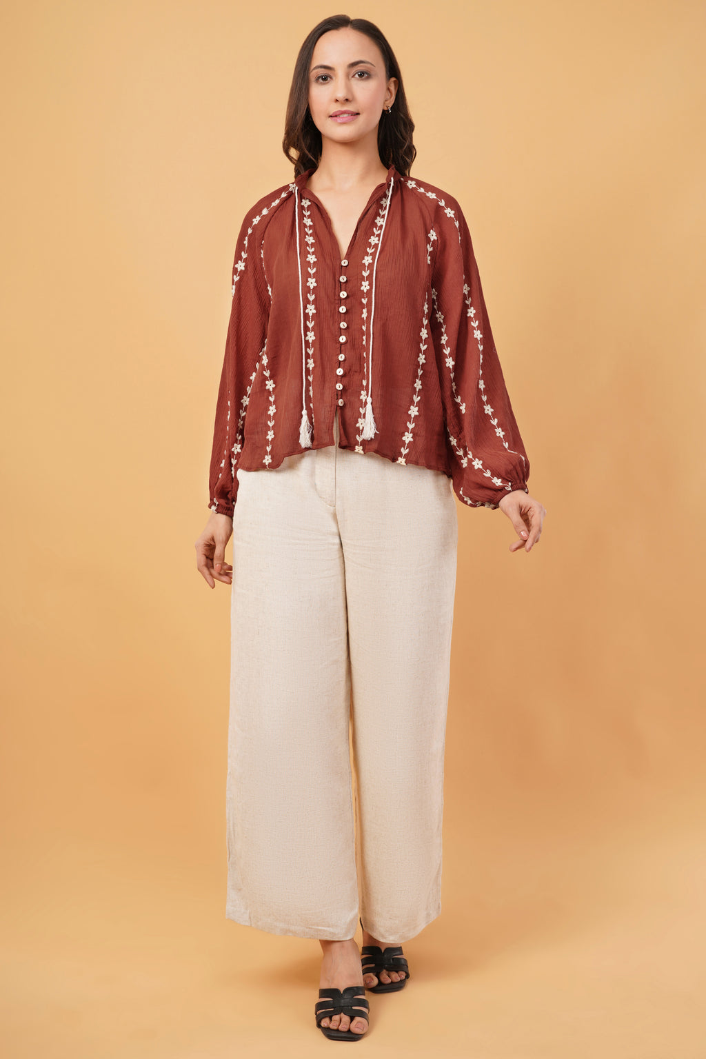 Woman wearing a red blouse with white patterns and beige pants on a beige background