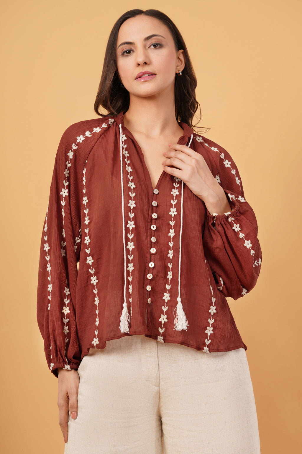 Woman wearing a rust-colored blouse with white floral embroidery on a beige background