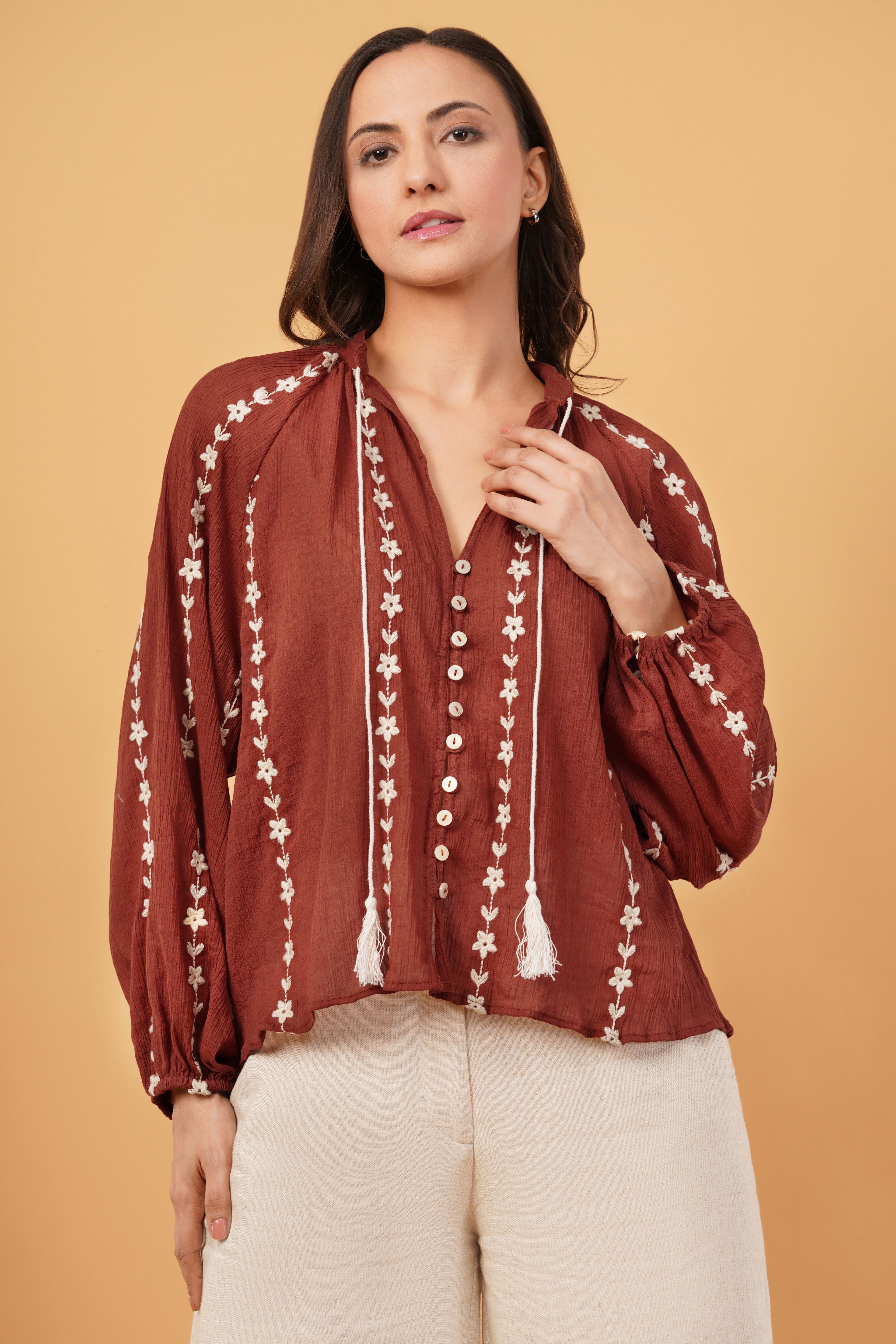 Woman wearing a rust-colored blouse with white floral embroidery on a beige background