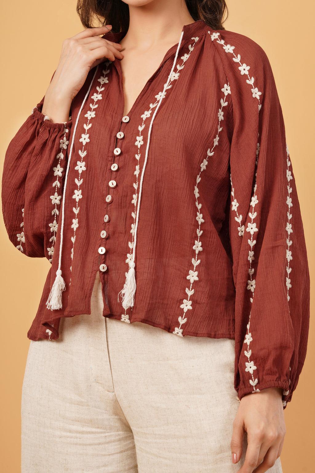 Red blouse with white embroidery and tassels on a beige background