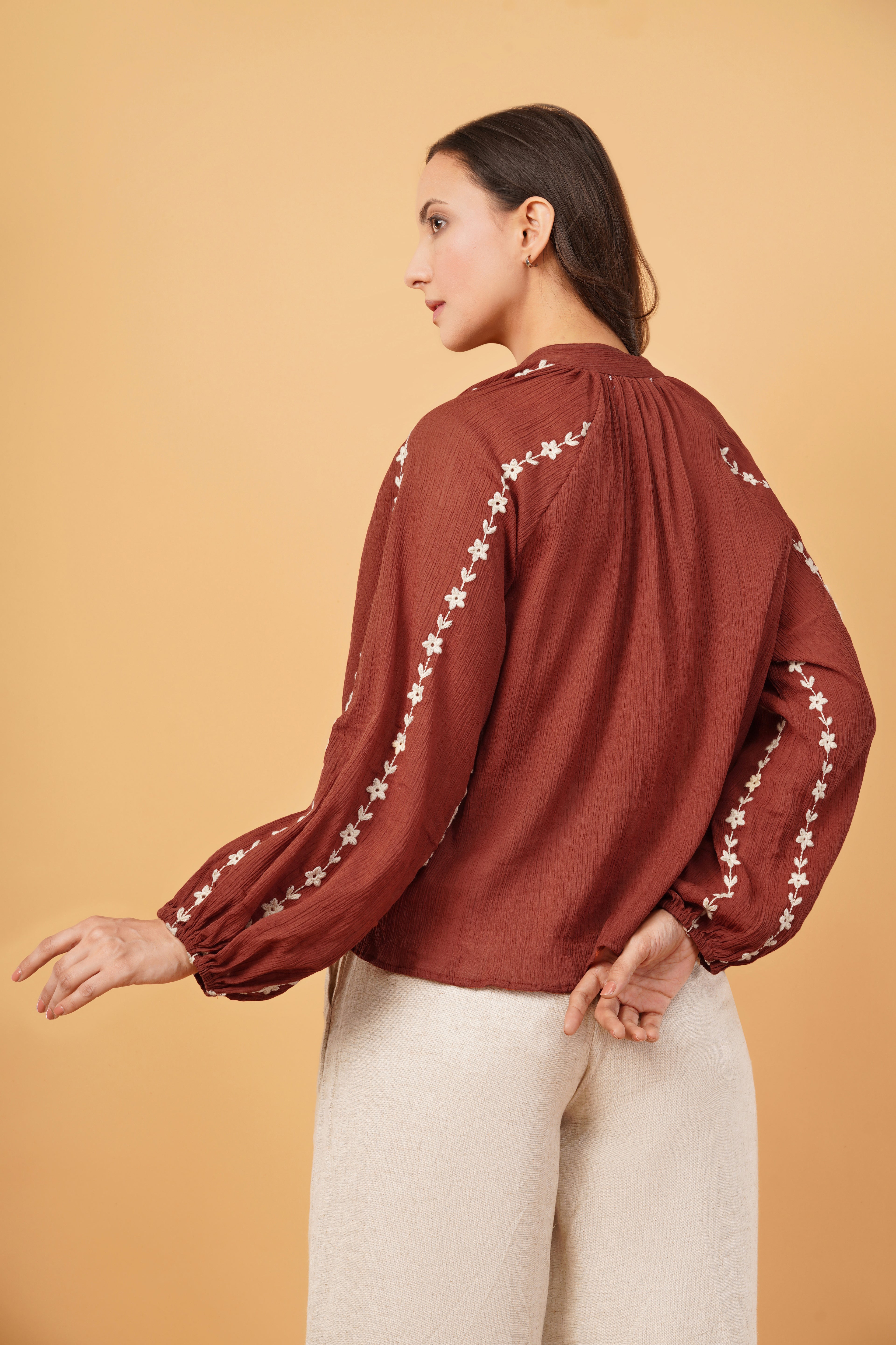 Woman wearing a burgundy blouse with floral embroidery on a beige background